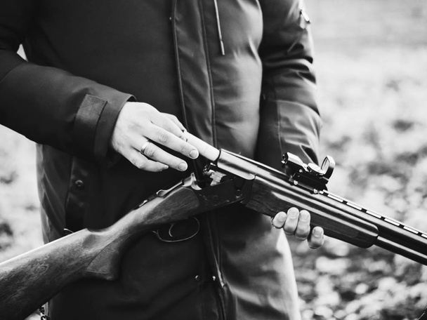 Humo de los troncos de un rifle de caza liso después de disparar. Hunter en camuflaje saca cartuchos de un arma. Blanco y negro
 - Foto, Imagen