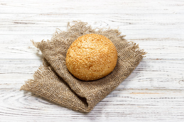 Fresh baked bread or bun with sesame and sunflower seeds on wooden table - 写真・画像