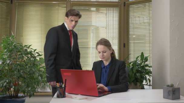 A young guy in a suit flirts with a girl in the office, gives her a green abloko, a girl works on a computer, a red laptop. 60 fps - Video
