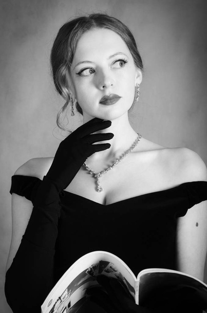 Girl in evening dress with magazine in hands. Black and white portrait in studio - 写真・画像