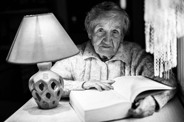 Fekete-fehér portré egy idős asszony, olvasson egy könyvet a éjszakai fény. - Fotó, kép