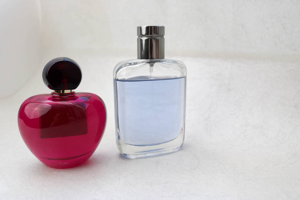 Two beautiful glass transparent shiny fashionable glamorous vials of cologne, perfume pink and blue with little caps and place for a simple text on a light white background. - Photo, Image