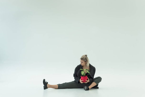 stylische Tänzerin allein sitzend mit roter Pflanze auf weißem Hintergrund - Foto, Bild