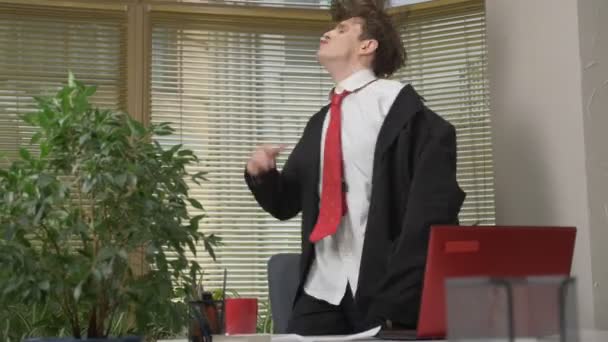 Young man in a suit dances in the office, makes funny faces, fools around, rejoices. Work in the office concept 60 fps - Materiał filmowy, wideo