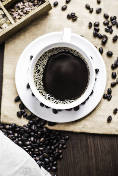 Чорна кава в білій чашці та кавовій квасолі на фоні дерева
. - Фото, зображення