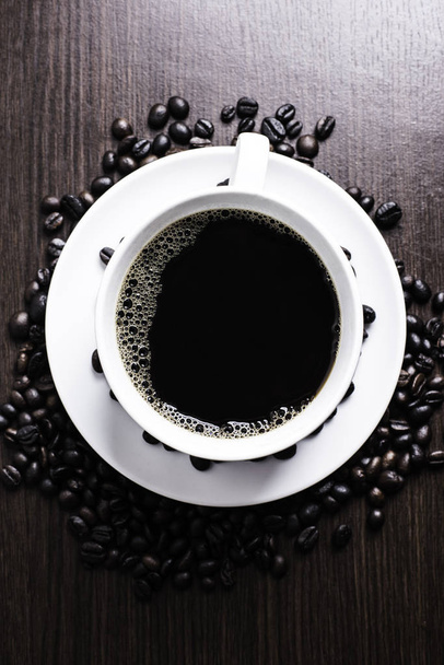 schwarzer Kaffee in weißer Tasse und Kaffeebohnen auf Holzhintergrund. - Foto, Bild