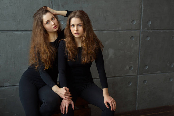 portrait of two beautiful young girls of twin sisters with flowing hair against the gray wall in the interior - Foto, Bild
