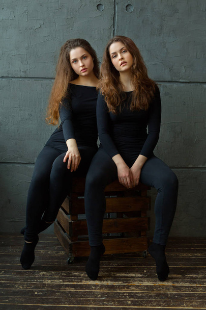 portrait of two beautiful young girls of twin sisters with flowing hair against the gray wall in the interior - Φωτογραφία, εικόνα