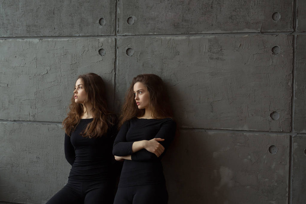 portrait of two beautiful young girls of twin sisters with flowing hair against the gray wall in the interior - 写真・画像