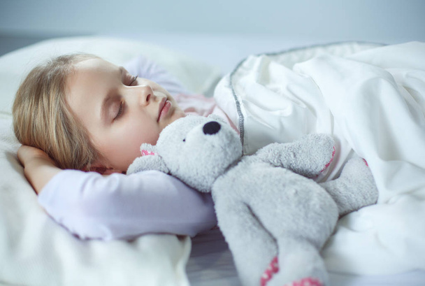 Child little girl sleeps in the bed with a toy teddy bear - Valokuva, kuva