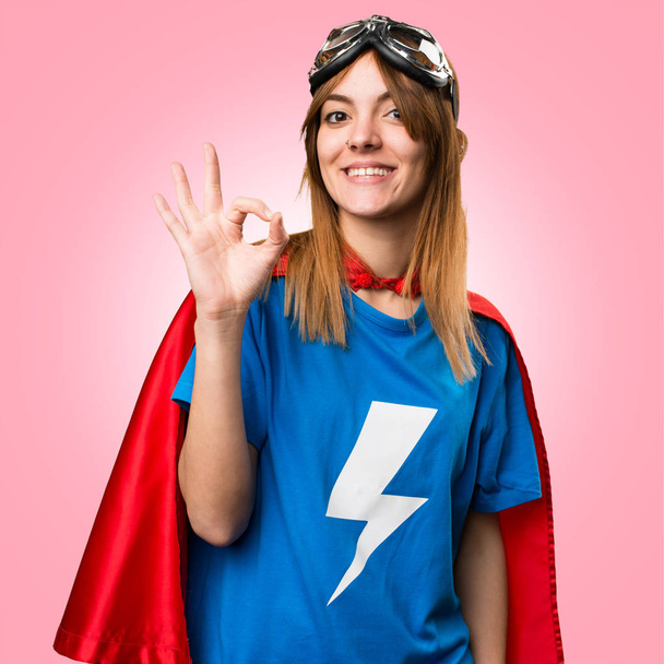 Αρκετά superhero κορίτσι κάνοντας Ok ναυτολογηθεί πολύχρωμο φόντο - Φωτογραφία, εικόνα