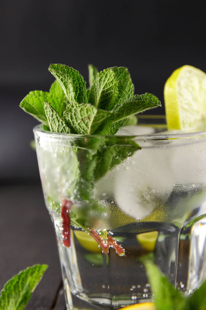 Mojito on a dark background, summer cocktail with lime and mint, refreshing drink with lemon, fresh mint for cocktail, celebratory drink with ice, vegan, copy space, minimalist cocktail, blank for designer, art - Photo, image