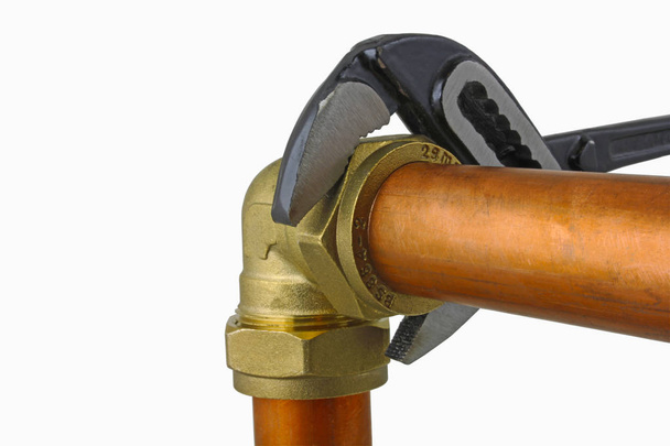 Clé réglable du plombier serrant la tuyauterie en cuivre Une clé réglable serrant un raccord de coude de compression à une tuyauterie en cuivre de 15 mm sur fond blanc
 - Photo, image