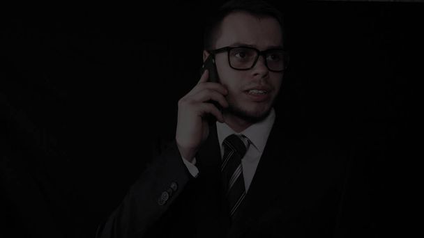 Handsome young businessman wearing glasses, talking on the phone in a suit, black background. - Fotografie, Obrázek