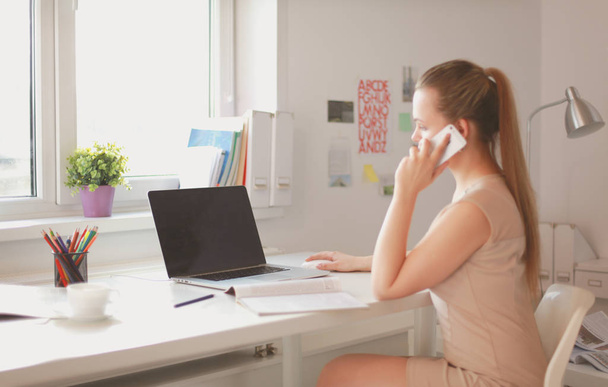 Young businesswoman sitting at the desk and talking on phone - Фото, зображення