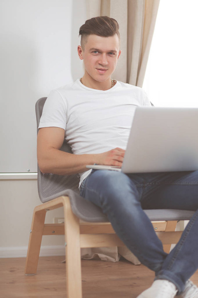 Jongeman zit op stoel met laptop - Foto, afbeelding