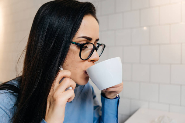 woman sitting in the office at the table and drinking coffee - Photo, image