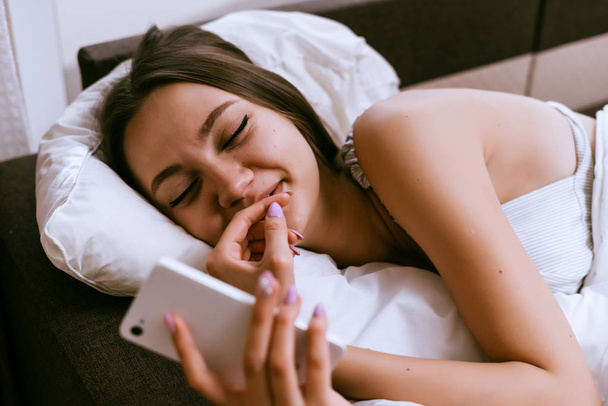 sleepy woman lies in bed and looks in phone - Foto, afbeelding