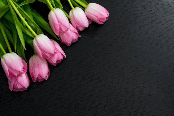 Σύνορα από φωτεινά ροζ τουλίπες λουλούδια σε μαύρο φόντο ξύλινη. - Φωτογραφία, εικόνα
