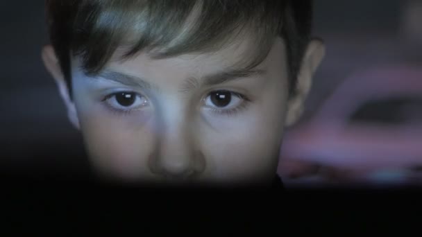 Nahaufnahme Gesicht des kleinen Jungen spielt Videospiel mit Laptop in dunklen Raum. Doppelbelichtung des Spiels im Gesicht und an der Wand. - Filmmaterial, Video
