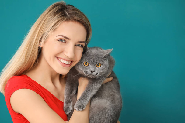 Young woman with cute pet cat on color background - Foto, Bild