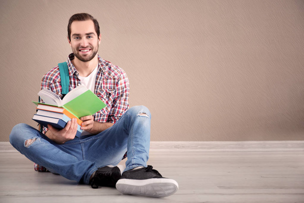 Student with notebooks sitting on floor against color wall - Photo, image