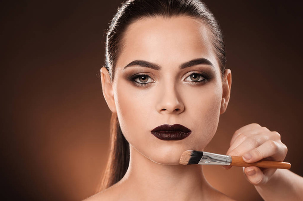 Professional visage artist applying makeup on woman's face against dark background - Foto, Imagen