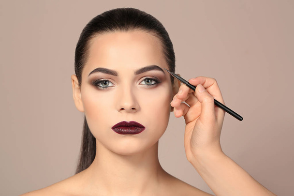 Professional visage artist applying makeup on woman's face against light background - Fotografie, Obrázek