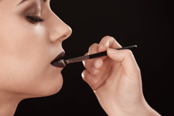 Professional visage artist applying makeup on woman's face against black background - Foto, Imagen