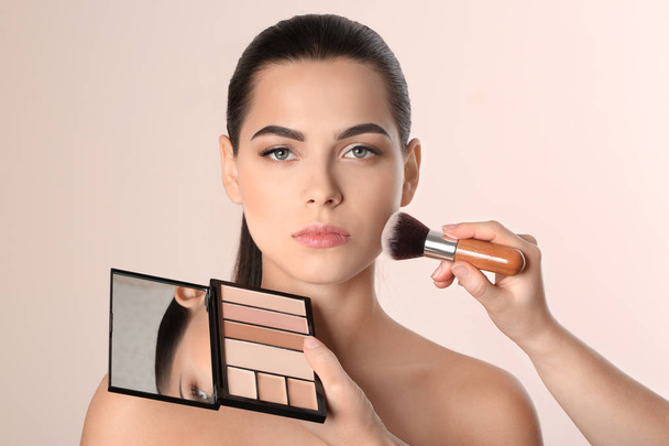 Professional visage artist applying makeup on woman's face against light background - Foto, Imagen