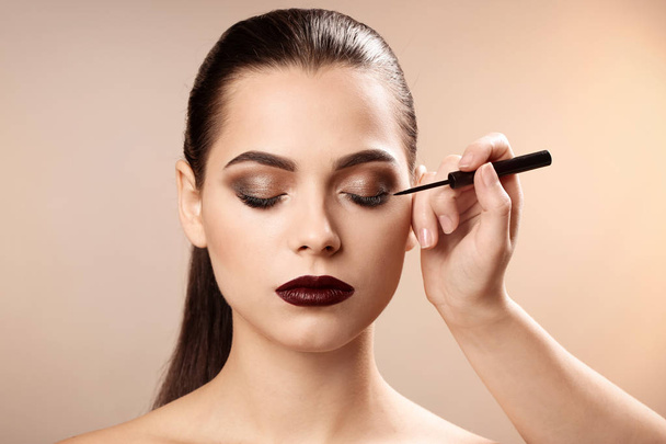 Professional visage artist applying makeup on woman's face against light background - Foto, Imagen