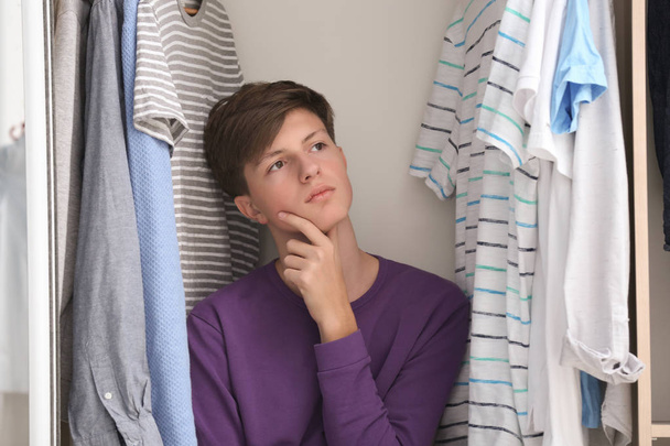 Thoughtful teenager among clothes in wardrobe - Фото, изображение