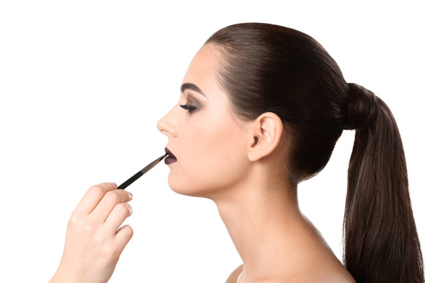 Επαγγελματική visage καλλιτέχνης εφαρμογή μακιγιάζ στο πρόσωπό της γυναίκας ενάντια σε λευκό φόντο - Φωτογραφία, εικόνα