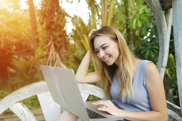 Blonde woman typing laptop, background of sunshine green palms in Thailand, Phuket travel - Photo, Image