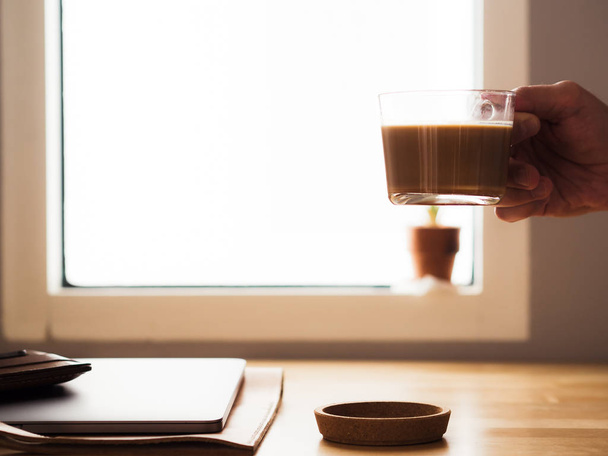 Drinking coffee on workspace desk with laptop by the window ligh - Фото, изображение