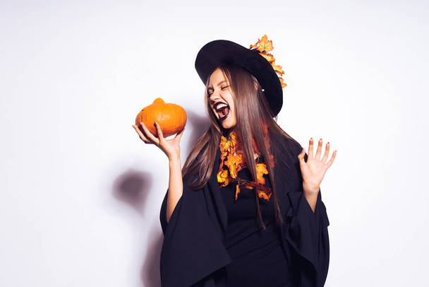 woman in a witch costume holds a pumpkin in her hands - Photo, Image