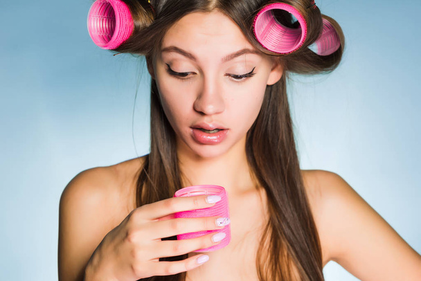 a woman on a blue background is surprised to take off the curlers - Foto, Bild