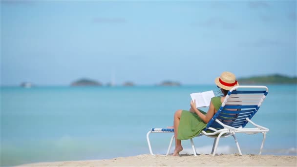 Nuori nainen lukemassa kirjaa leposohvasta trooppisella valkoisella rannalla
 - Materiaali, video