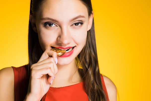 woman on a yellow background gnawing a coin - Photo, Image
