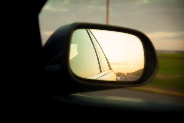 Δρόμος προβληματισμού με οδική γραμμές πάνω από το ηλιοβασίλεμα από την πλευρά του καθρέφτη πίσω όψη του κινούμενου αυτοκινήτου - Φωτογραφία, εικόνα