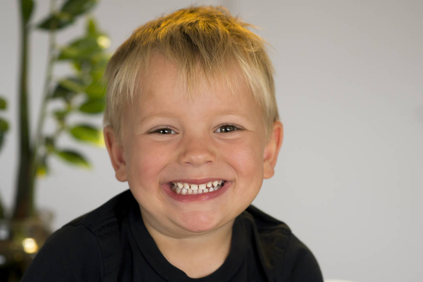  portrait of blond beautiful 3 or 4 years old caucasian kid smiling happy in joyful face expression isolated at home looking to camera - Photo, Image