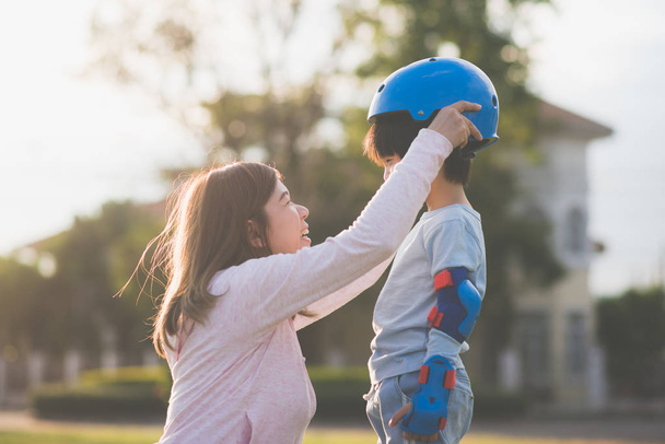 Asiática madre ayudando a su hijo lleva casco azul en disfrutar de tiempo juntos en el parque
 - Foto, imagen