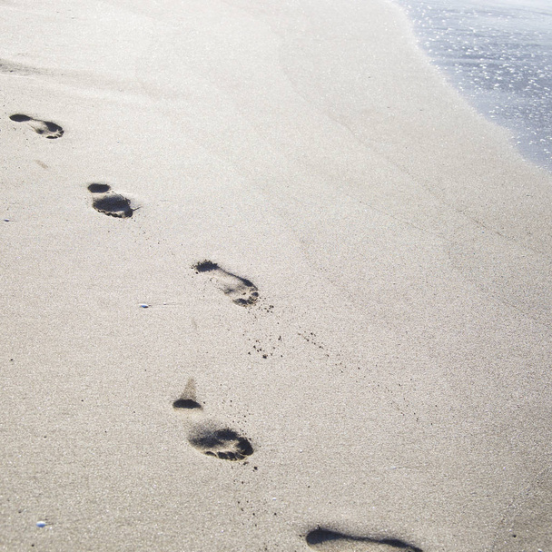 Ślady stóp na piasku nad morzem. Lato Plaża wakacje koncepcja. Sezonowe wyjazdy do morza lub oceanu. Tło - Zdjęcie, obraz