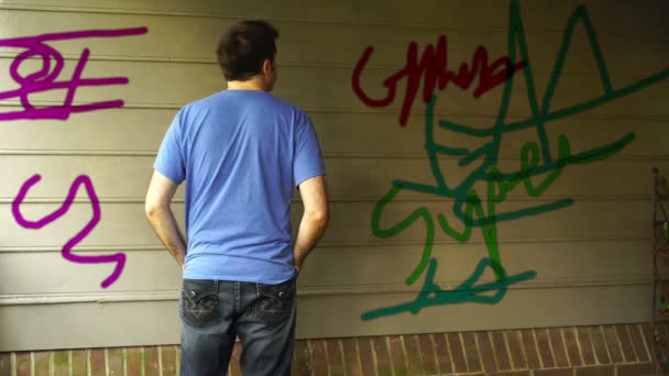 Mies katselee graffiteja rakennuksen ulkopuolella
 - Materiaali, video