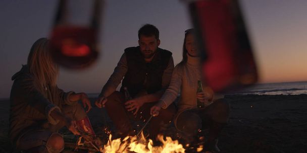 Group of young people having fun at beach around bonfire on sunset - Valokuva, kuva