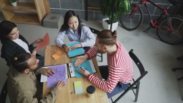 Bovenaanzicht van start-up bedrijf biedt multi-etnische team zitten aan de tafel met projectdocumenten en chatten tijdens de koffiepauze in gezellige kantoor - Video