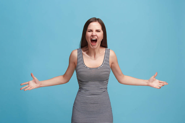The young emotional angry woman screaming on blue studio background - 写真・画像