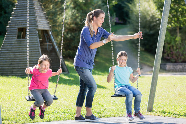 Famille avec deux filles et mère sur aire de jeux swing
 - Photo, image