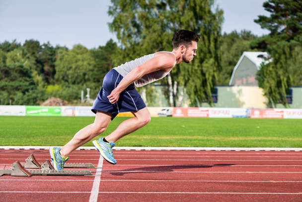 Спортсмен на шлакобежной дорожке спортивного объекта начинает спринт
 - Фото, изображение