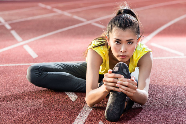 Woman athlete stretching on racing track before running - Photo, Image